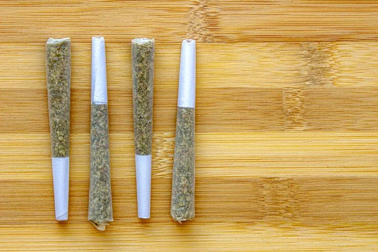 Four neatly rolled cannabis pre-rolls placed side by side on a wooden table.