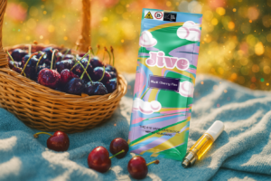 Jive Black Cherry Fizz vape cartridge next to its packaging, resting on a picnic blanket with a woven basket of juicy, dewy cherries in the midground, evoking a fresh, flavorful outdoor vibe.
